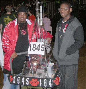 The team operates the robot by joysticks and a digital radio remote control from behind a clear panel next to the court.